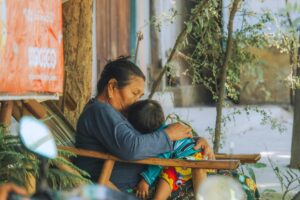 A Burmese grandmother lovingly embraces her grandchild in a peaceful outdoor setting.